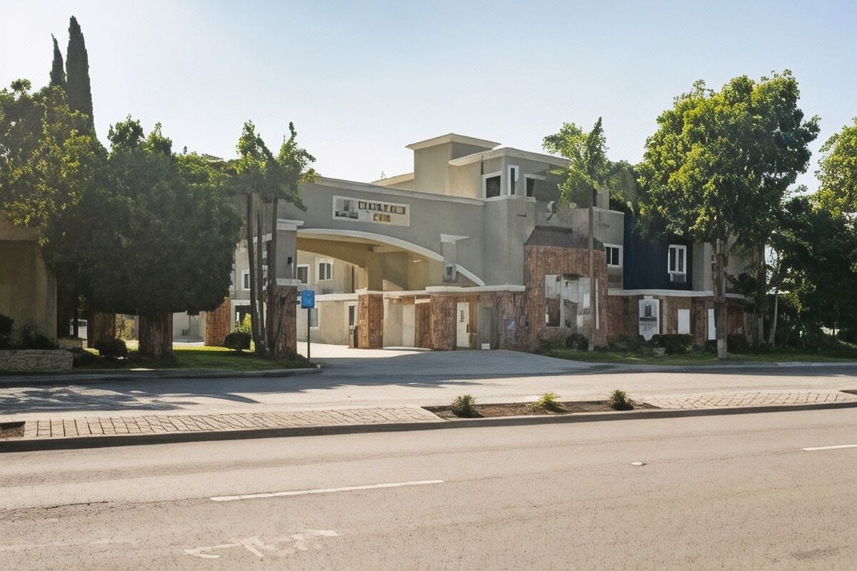 A multi-story hotel with a prominent entrance, a parking lot, and a landscaped area with trees.