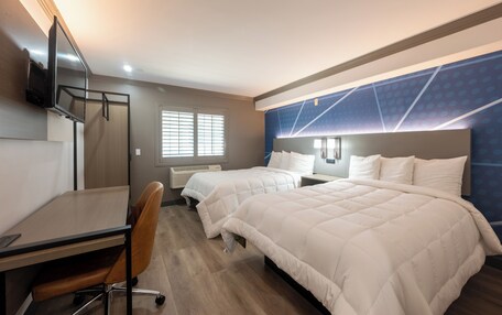 A hotel room with two beds, a desk, a chair, a TV, and a window with blinds.