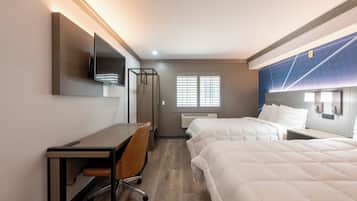 A hotel room with a desk, chair, two beds, a TV, and a window with blinds.