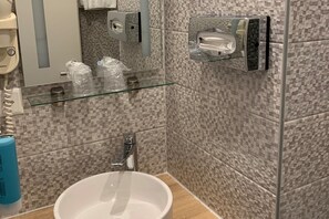 A bathroom with a glass shelf holding toiletries, a sink, and a mirror. - Admiral Hotel (Geneva)