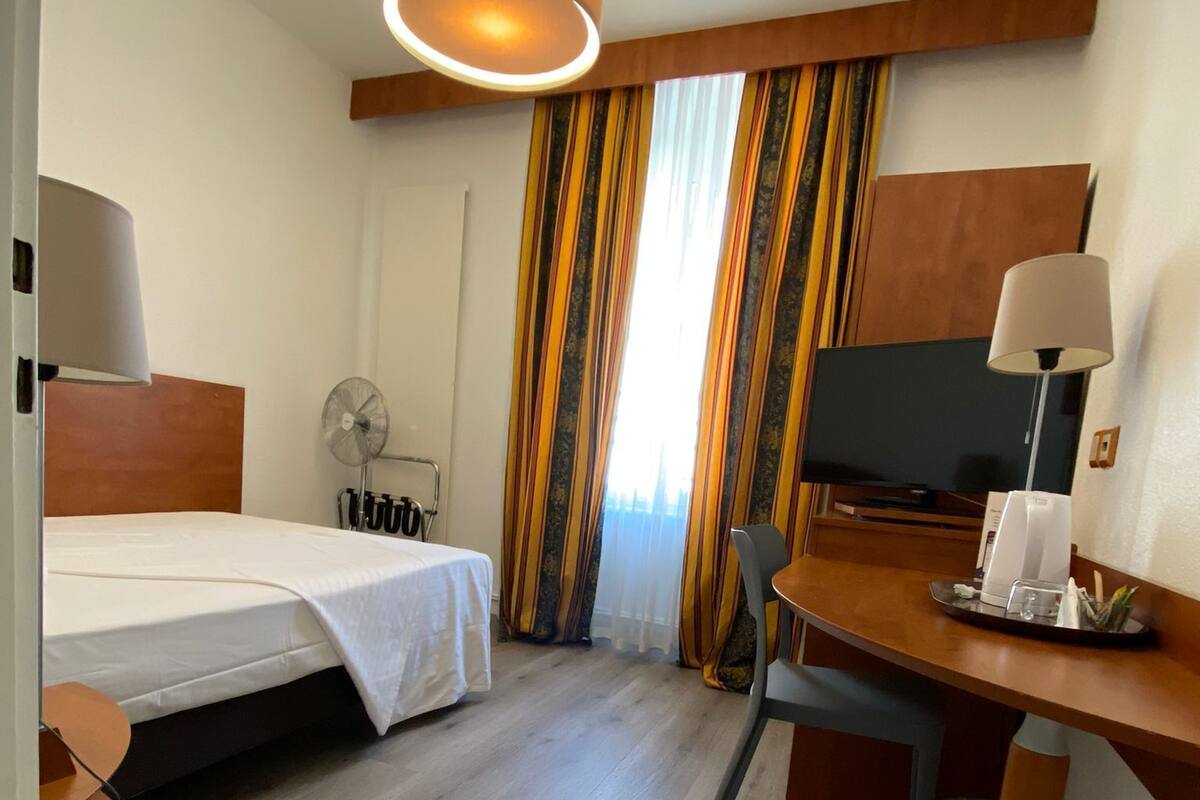Habitación de hotel con cama, escritorio, silla, televisor y cortinas.