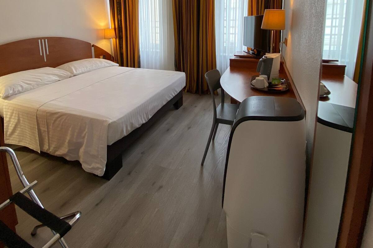 Una habitación de hotel con cama, escritorio, silla, lámpara y cortinas.