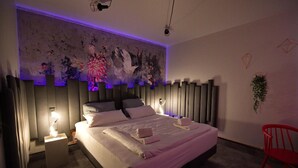 A modern bedroom with a large bed, bedside lamps, a red chair, and a wall-mounted plant. - Hotel Mecklenheide Hannover (Hannover)