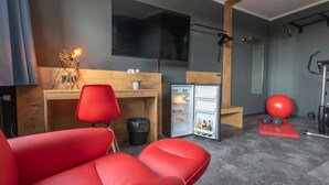 A modern room with a red sofa, a small wooden desk, a refrigerator, a TV, and a pull-up bar. - Hotel Mecklenheide Hannover (Hannover)