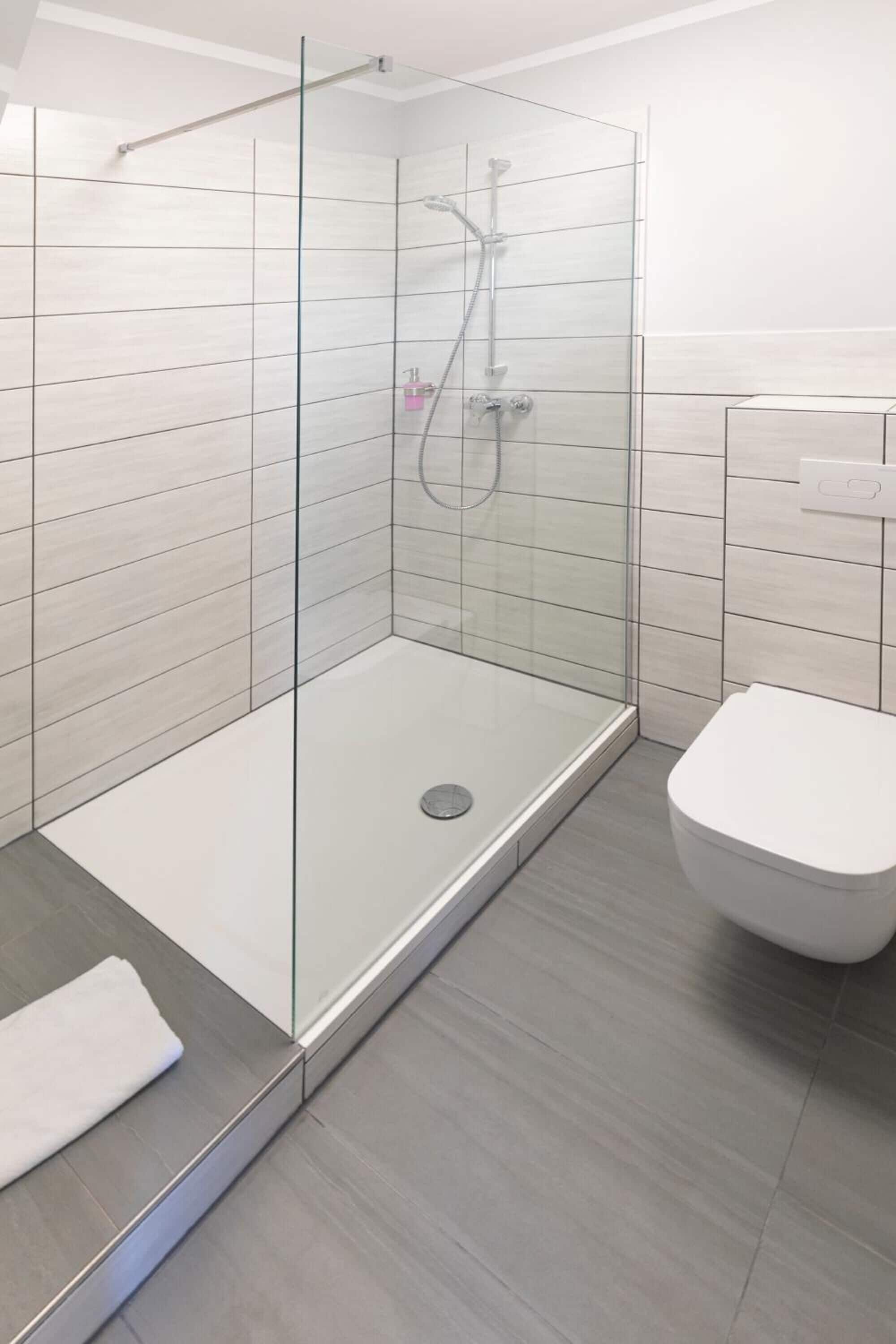 Un baño moderno con ducha de vidrio, inodoro blanco y paredes cubiertas de baldosas claras.