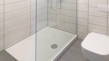 Un baño moderno con ducha de vidrio, inodoro blanco y paredes cubiertas de baldosas claras.
