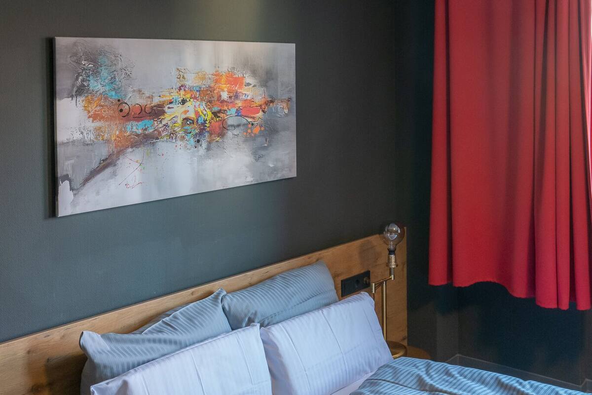 A neatly made bed with striped bedding, a wooden headboard, and a modern abstract painting on the wall.