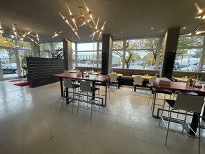 A modern restaurant interior with high ceilings, pendant lighting, and large windows offering views of the street. - Hotel Mecklenheide Hannover (Hannover)