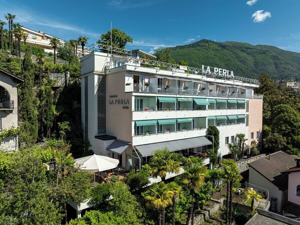 Un hôtel à plusieurs étages, appelé « La Perla », doté de balcons, d’un espace extérieur aménagé et entouré d’une végétation luxuriante.