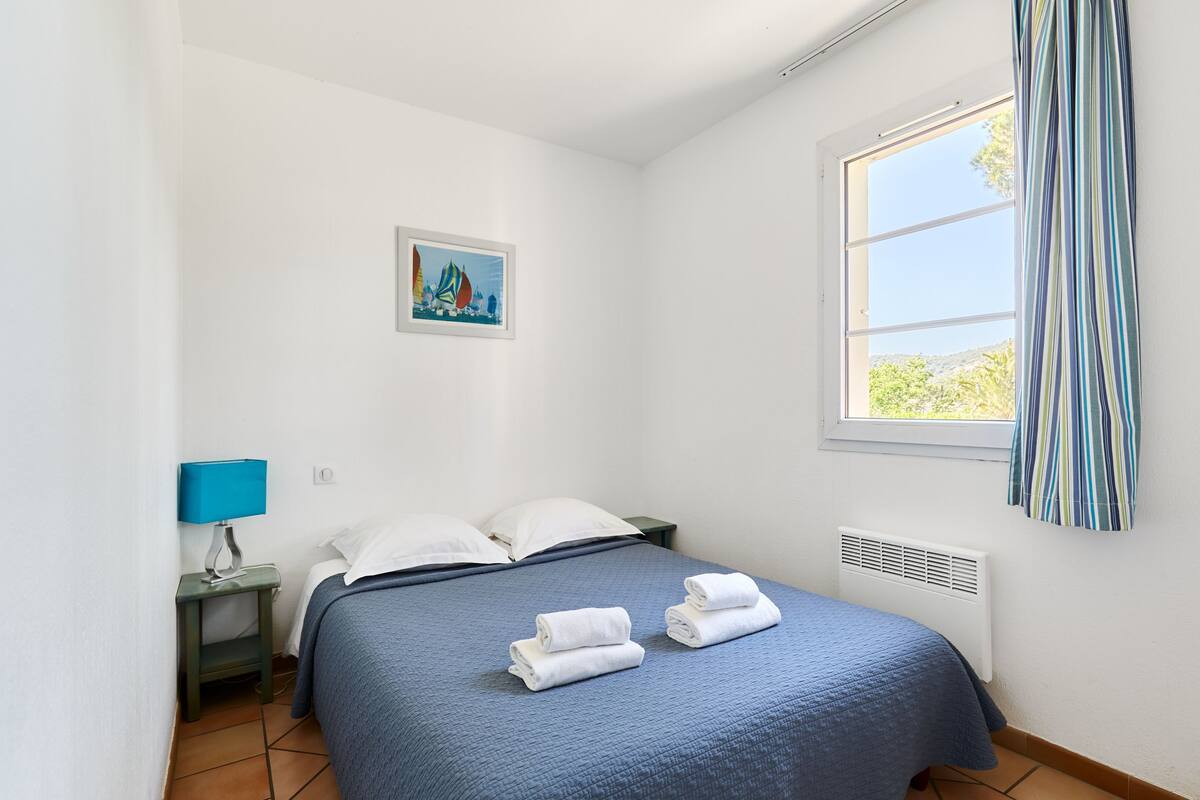 A neatly made bed with blue bedding, white pillows, and two folded towels on the bed.