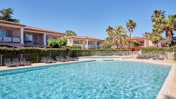 A swimming pool with lounge chairs, palm trees, and a building with a red-tiled roof.