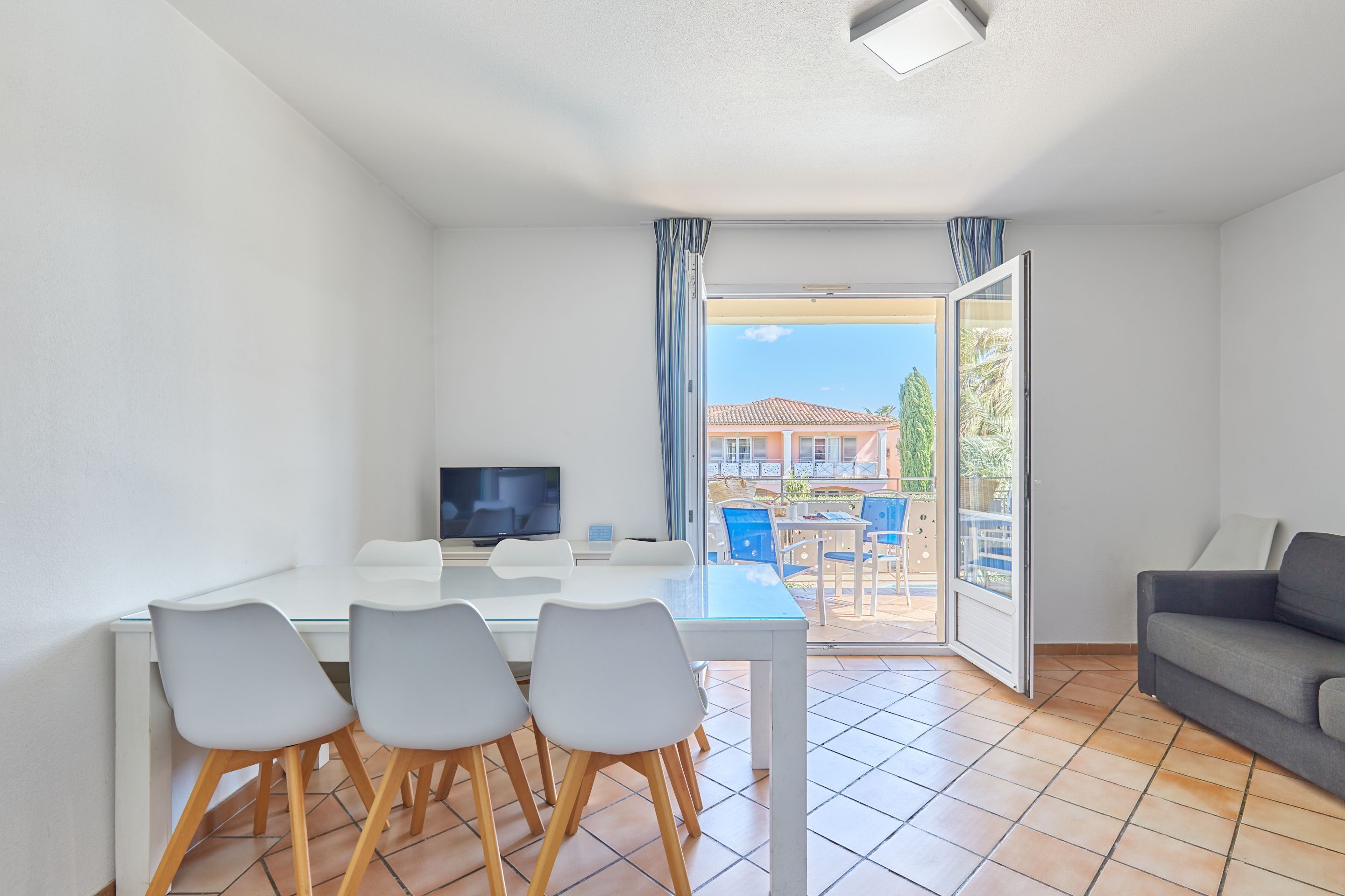 A modern room with a dining table, chairs, a sofa, a TV, and a sliding glass door to an outdoor area.