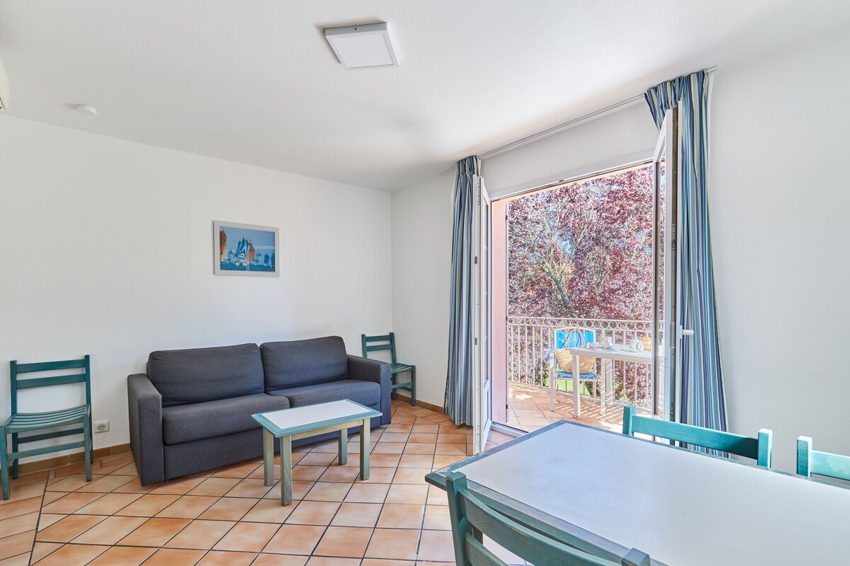 Un salón con sofá, una mesita y un balcón con vistas a árboles.