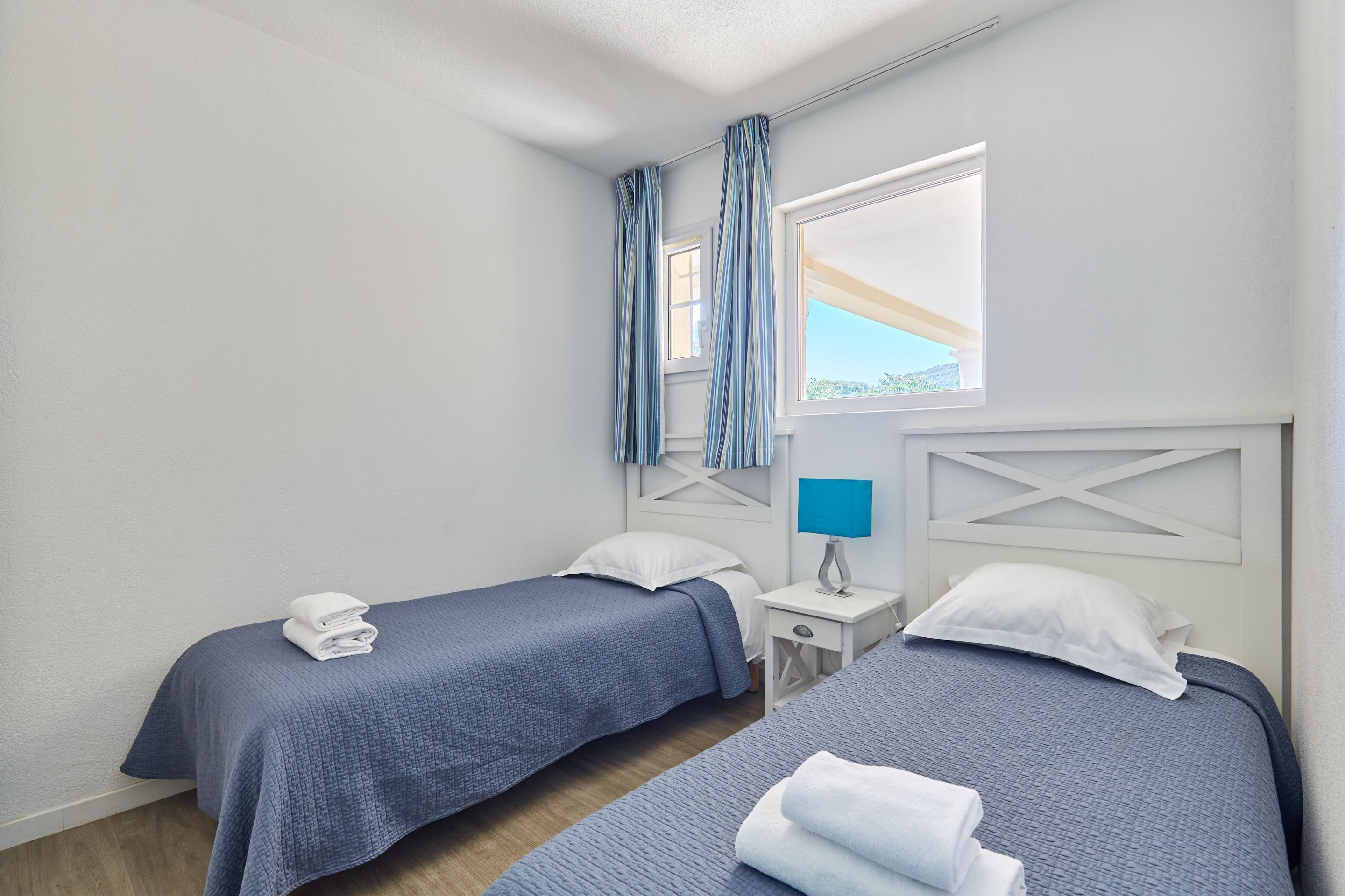 Hotelkamer met twee bedden, een raam met gordijnen, een nachtkastje met lamp en uitzicht op de omgeving.