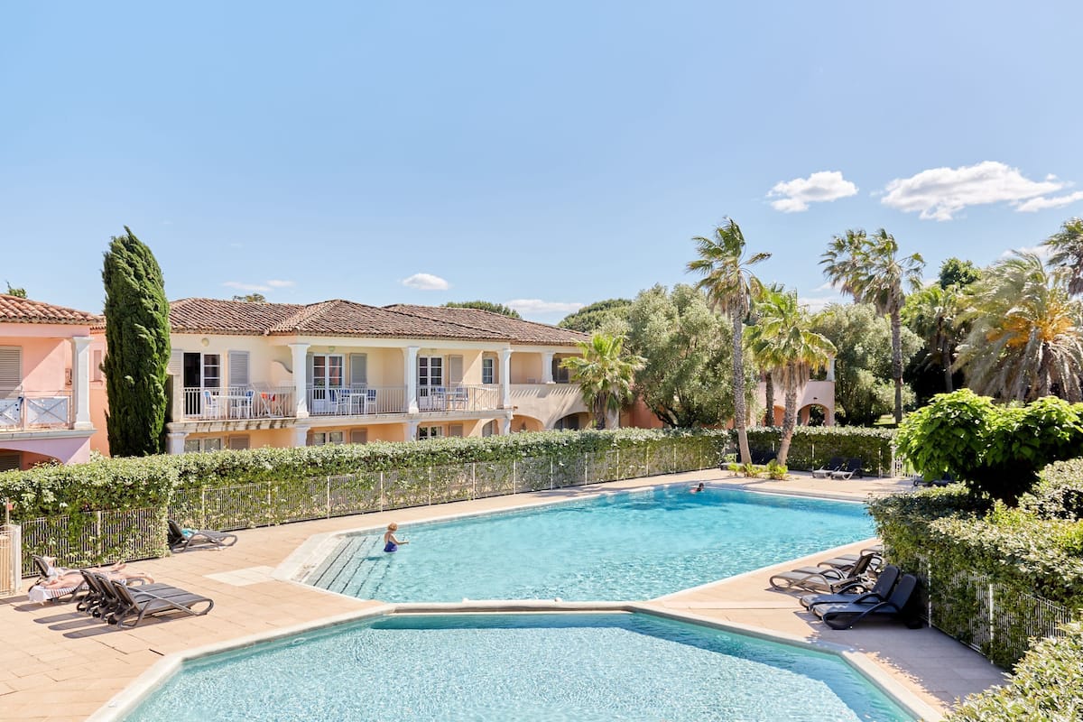 A swimming pool with lounge chairs, a building with balconies, and palm trees.