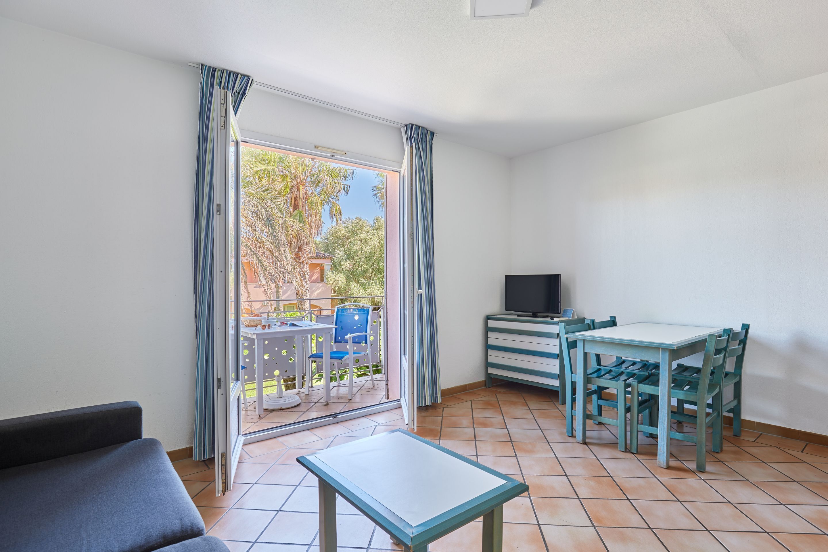 Una habitación con una mesa de comedor, sillas, un sofá, un televisor y un ventanal corredizo que da a un espacio exterior con una mesa y sillas.