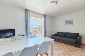 Habitación de hotel con una mesa de comedor, sillas, televisor de pantalla plana, sofá y balcón con cortinas.