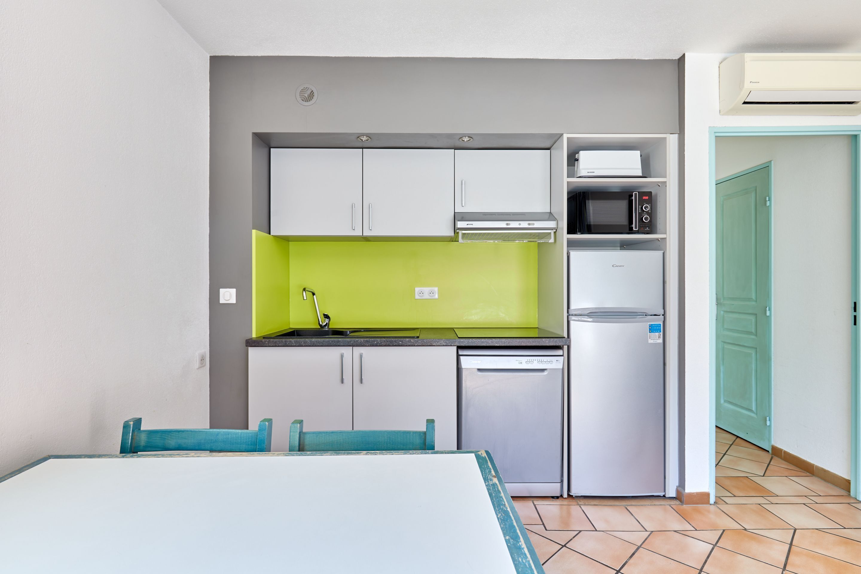 A compact kitchen with a microwave, oven, and dishwasher, a dining table with chairs, and a green accent wall.