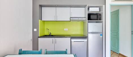 A compact kitchen with a microwave, oven, and dishwasher, a dining table with chairs, and a green accent wall.