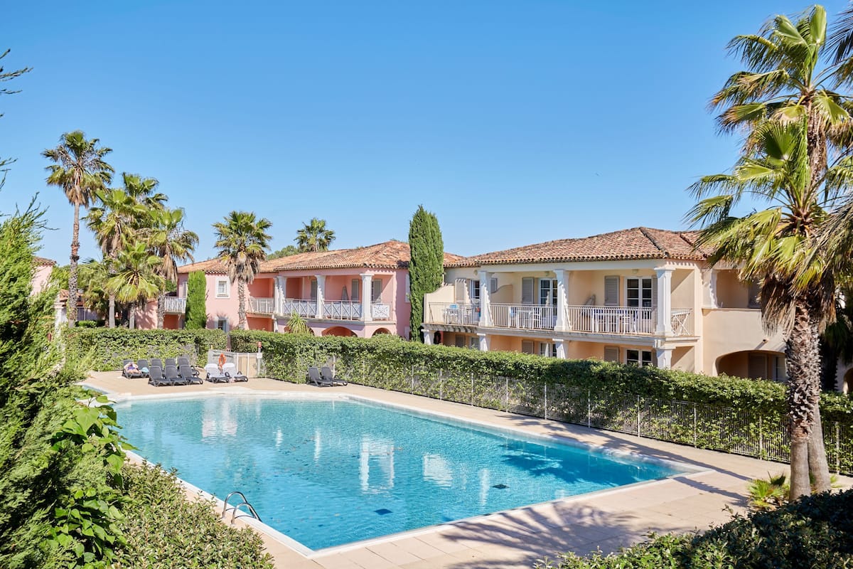 A swimming pool surrounded by palm trees and a row of buildings with balconies.