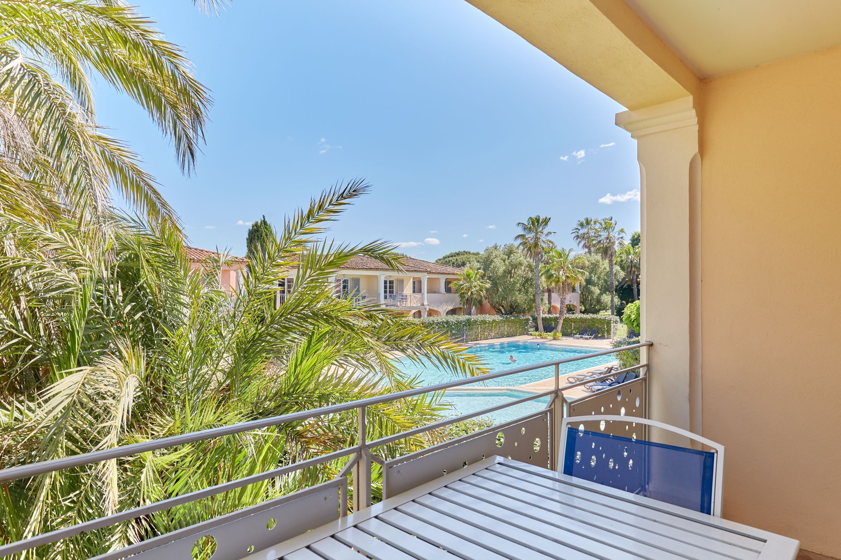 A balcony with a view of a swimming pool, palm trees, and a building in the background.