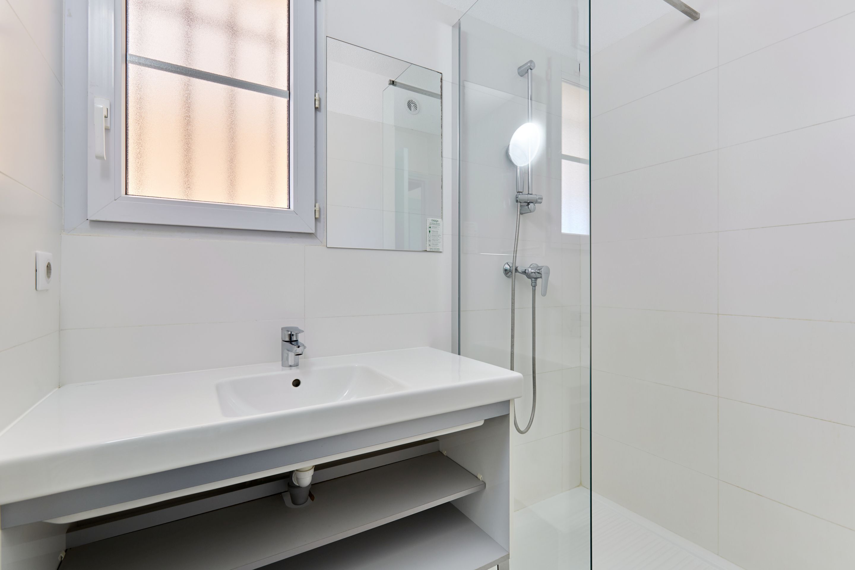 A modern bathroom with a white sink, a mirror, and a glass-enclosed shower.