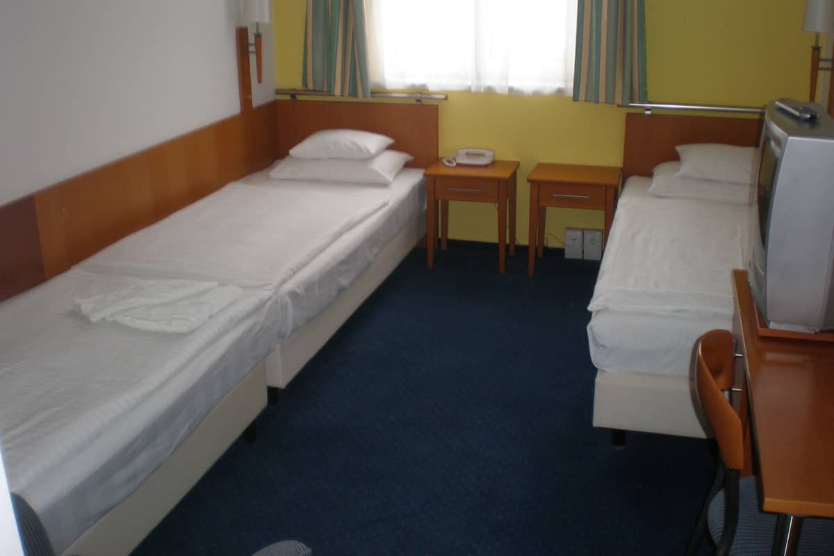 A hotel room with two single beds, a small table, a chair, and a television.