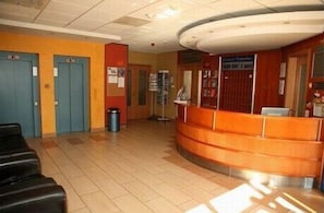 A reception area with a curved orange counter, a trash bin, and a bulletin board. - Hotel Veritas (Budapest)