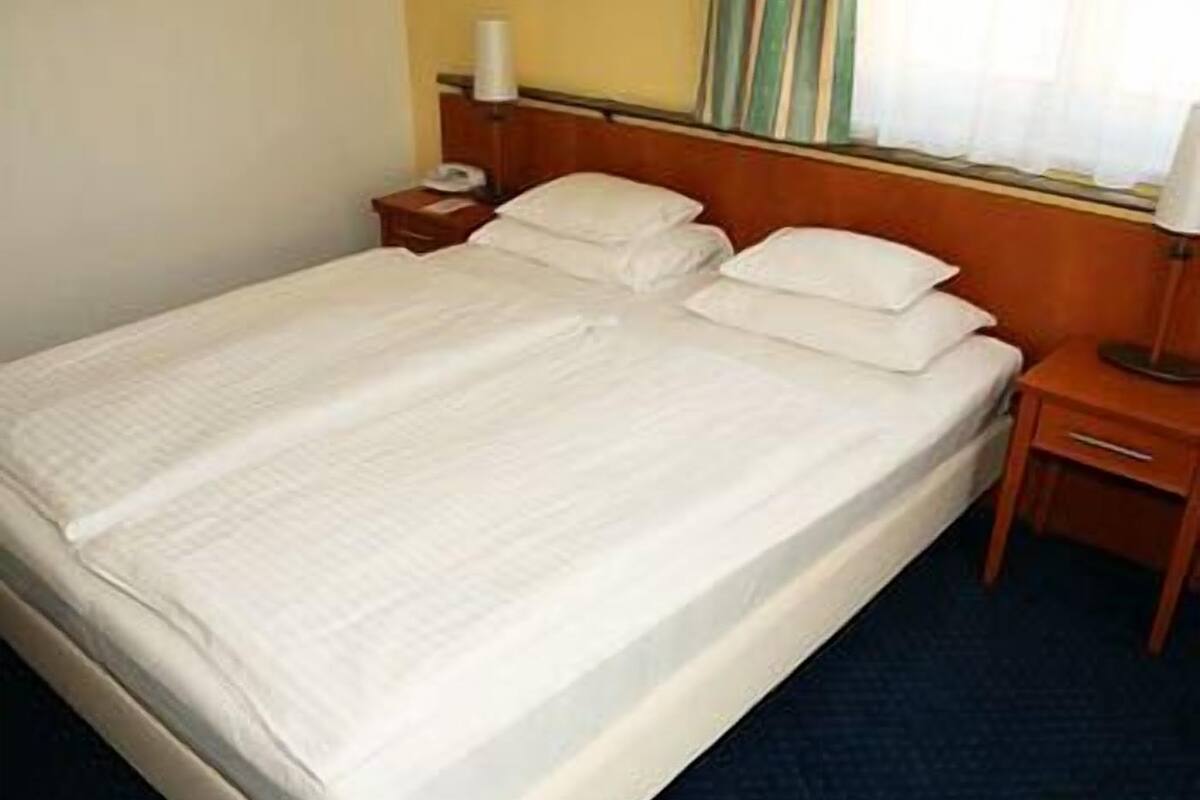A neatly made bed with white linens in a hotel room.