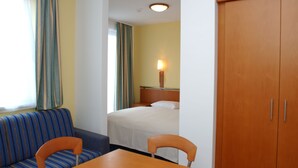 Ett hotellrum med en säng, en garderob i trä, en soffa, ett bord och en lampa.