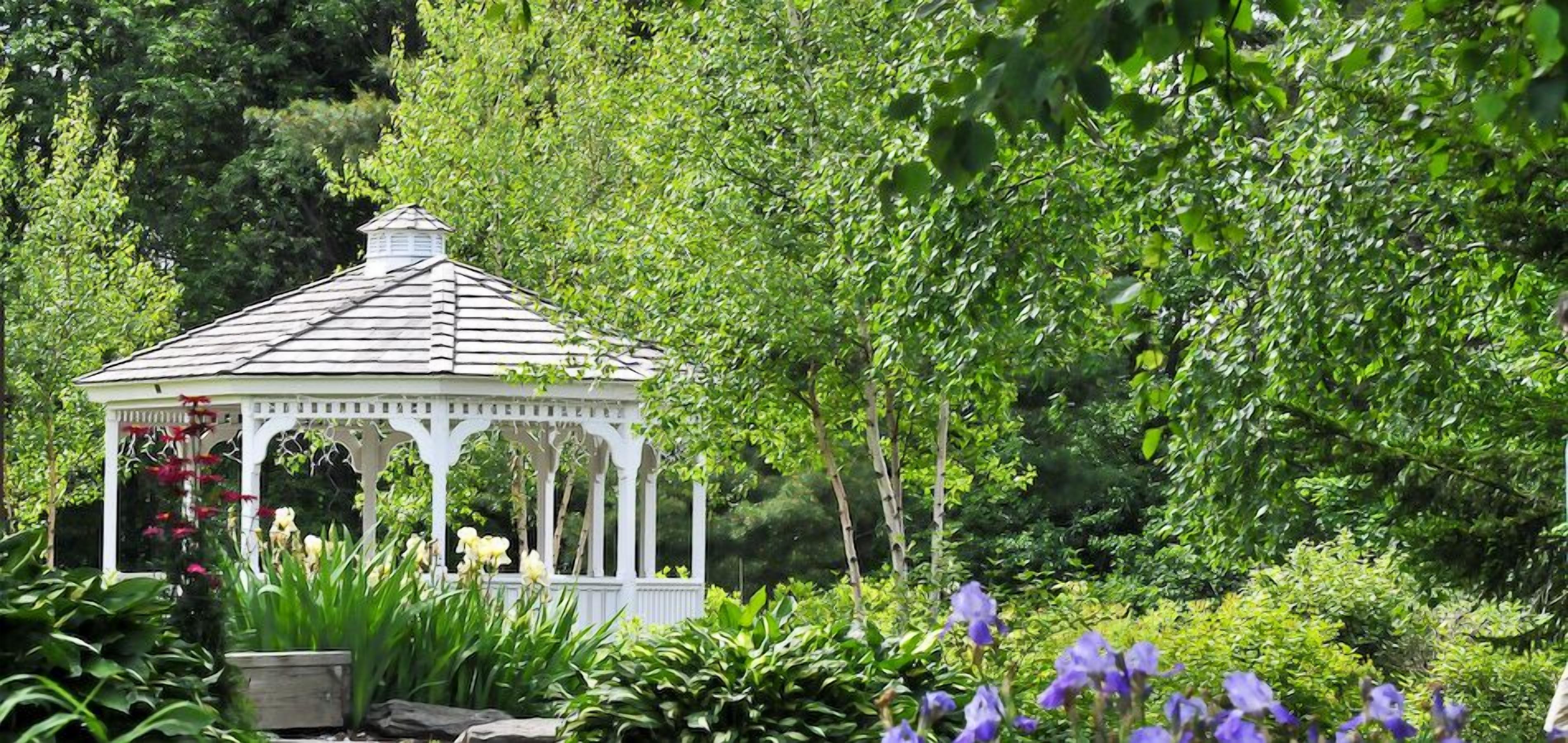 A white gazebo surrounded by lush greenery and flowers.