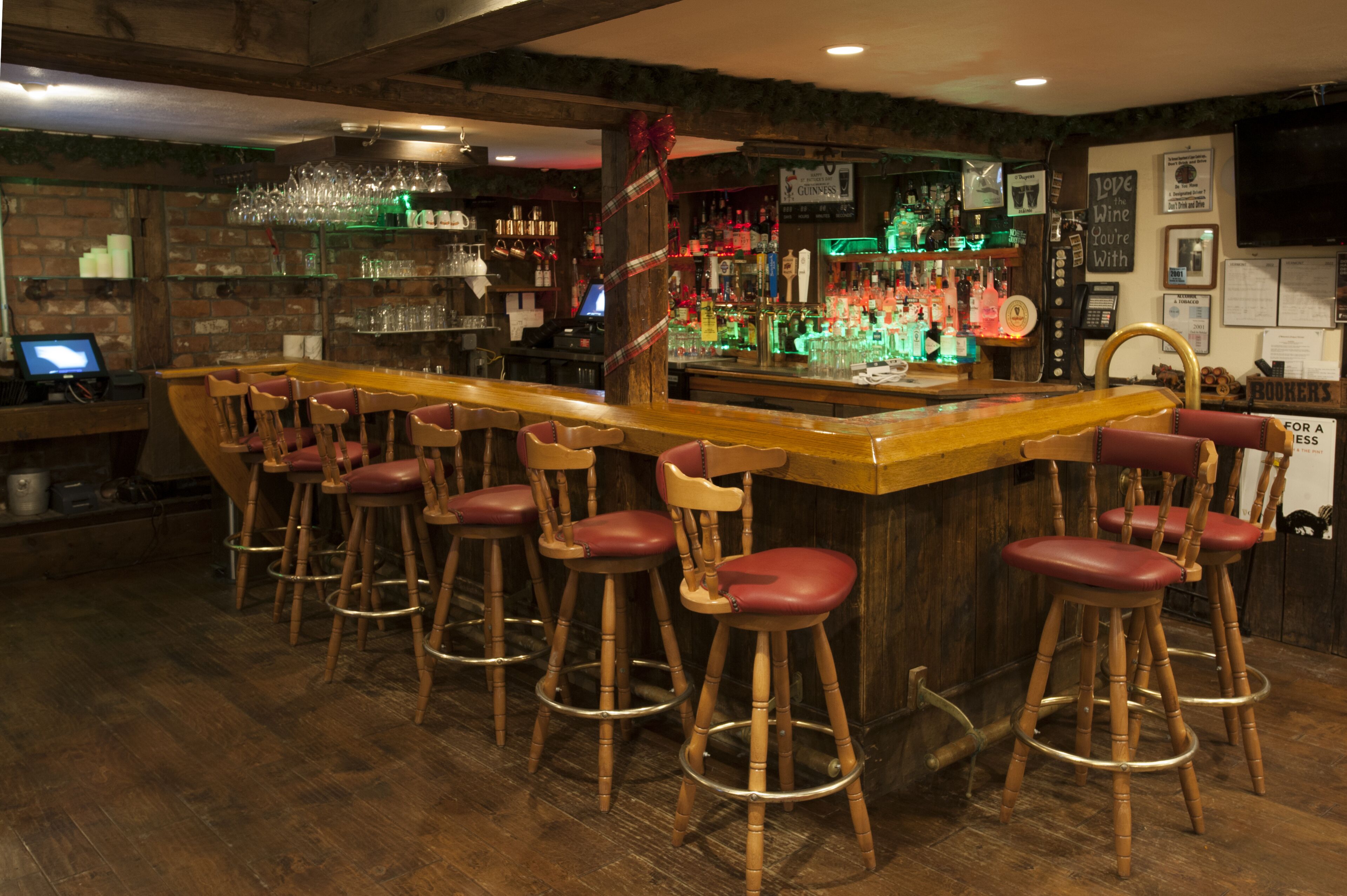 A bar area with wooden stools, a bar counter, and shelves stocked with bottles.