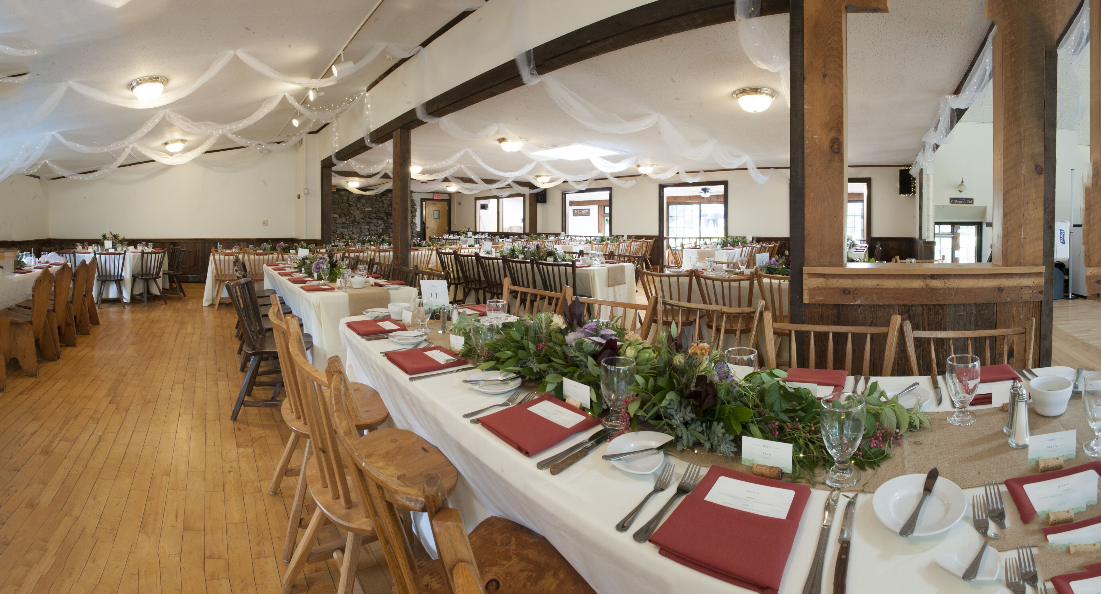 A banquet hall with long tables set for a formal event, wooden chairs, and a stone wall in the background.