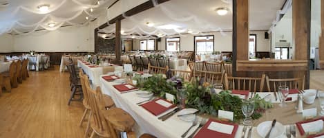 A banquet hall with long tables set for a formal event, wooden chairs, and a stone wall in the background.