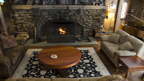 A cozy living room with a stone fireplace, a round wooden coffee table, and a beige sofa. - Summit Lodge (Killington)