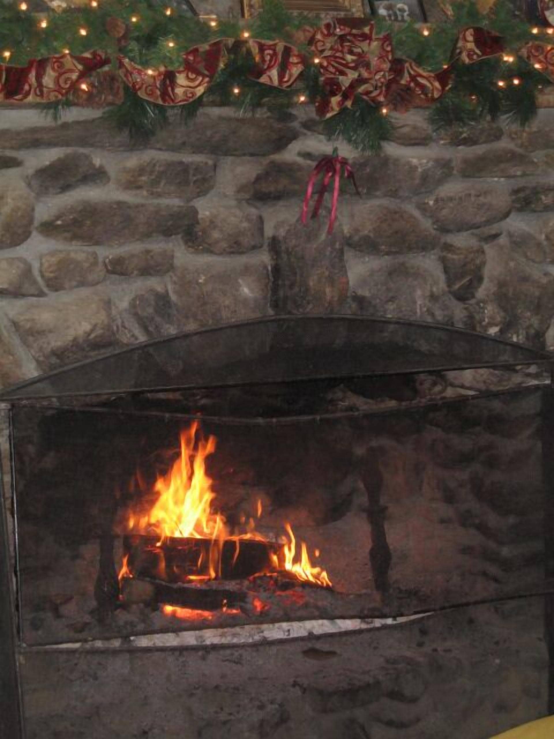 A stone fireplace with a fire burning inside, surrounded by festive garlands and a red ribbon.