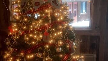 A decorated Christmas tree with lights and ornaments, placed in a room with a brick floor and a window with a view of buildings outside.