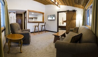 Una sala de estar acogedora con un sofá, un sillón, una mesa de centro de madera y un televisor montado en la pared.