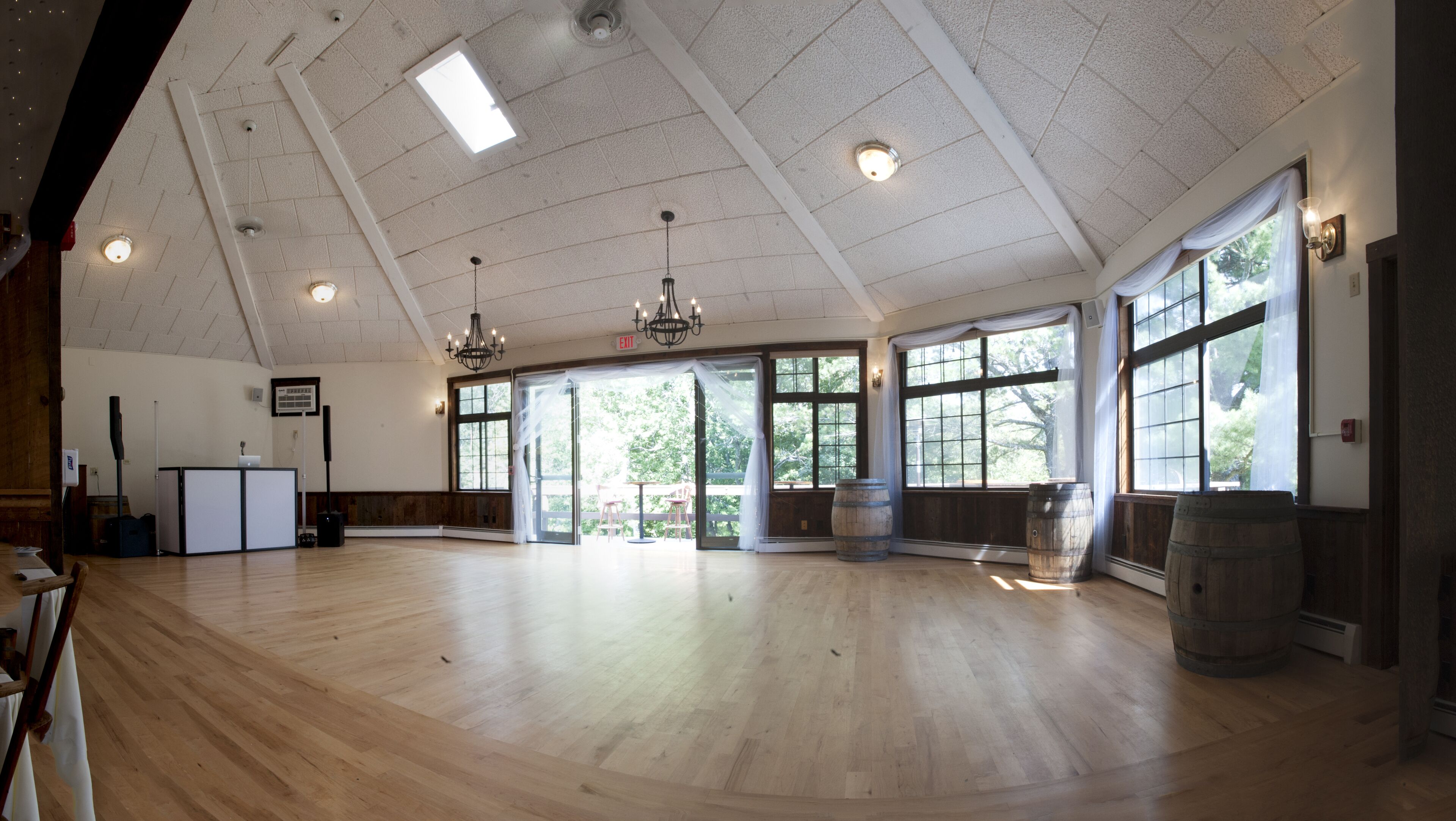 A spacious hall with wooden floors, large windows, and a chandelier.