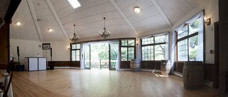 A spacious hall with wooden floors, large windows, and a chandelier.
