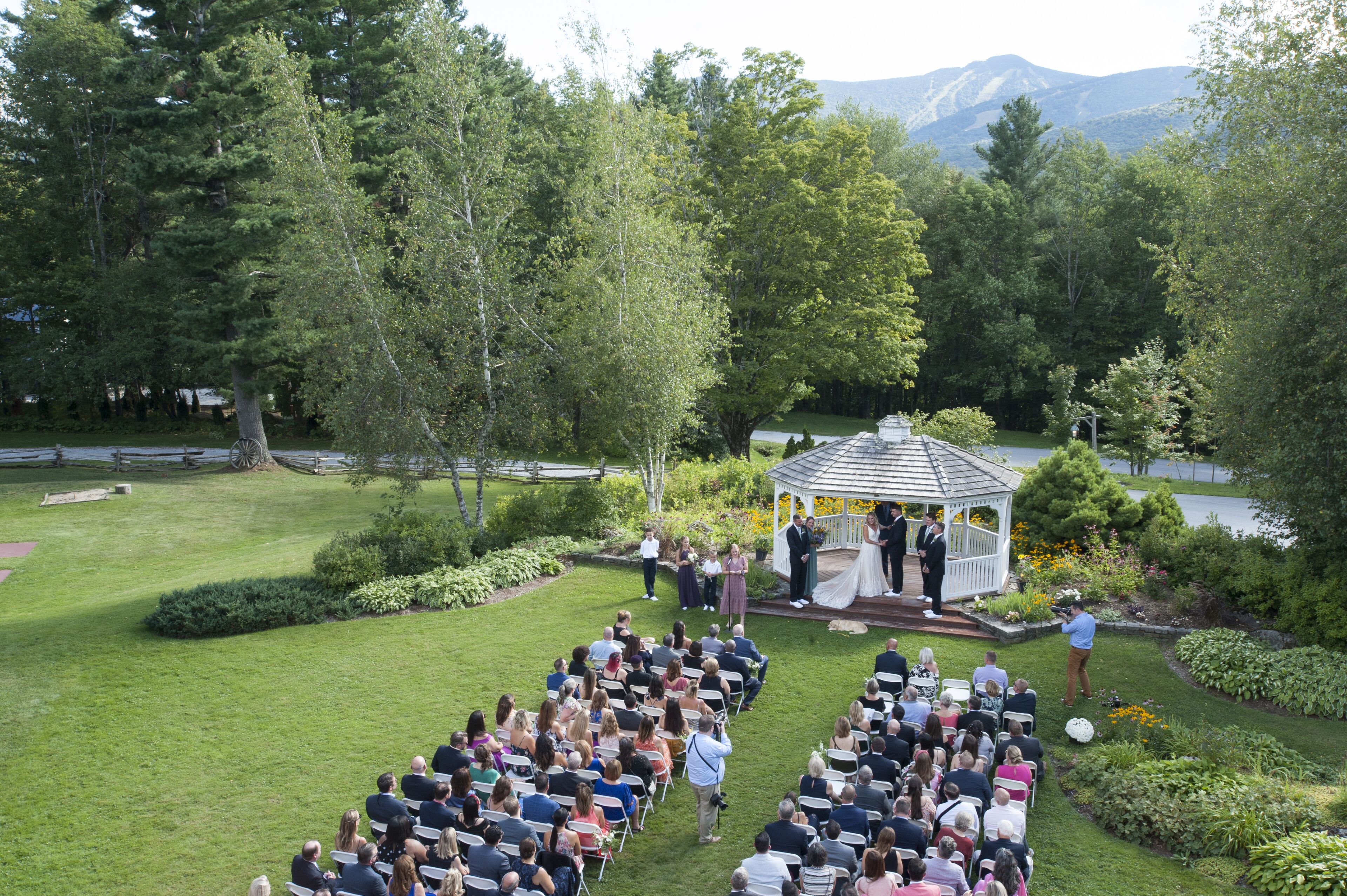 An outdoor wedding ceremony with guests seated in rows facing a gazebo.