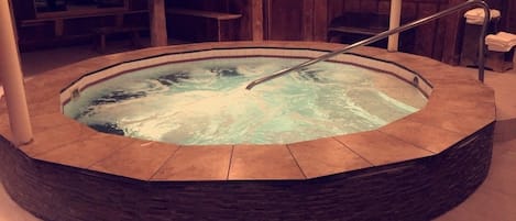 A circular hot tub with a metal railing, surrounded by stone tiles.