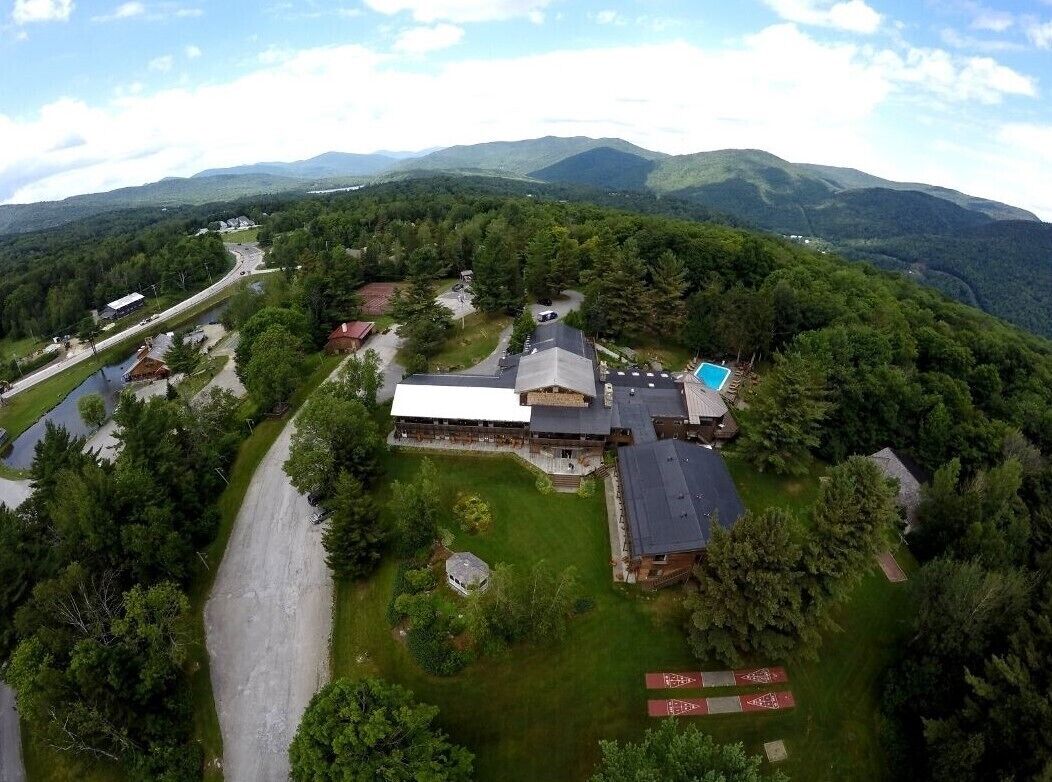 A large building with a swimming pool, surrounded by lush greenery and mountains in the background.