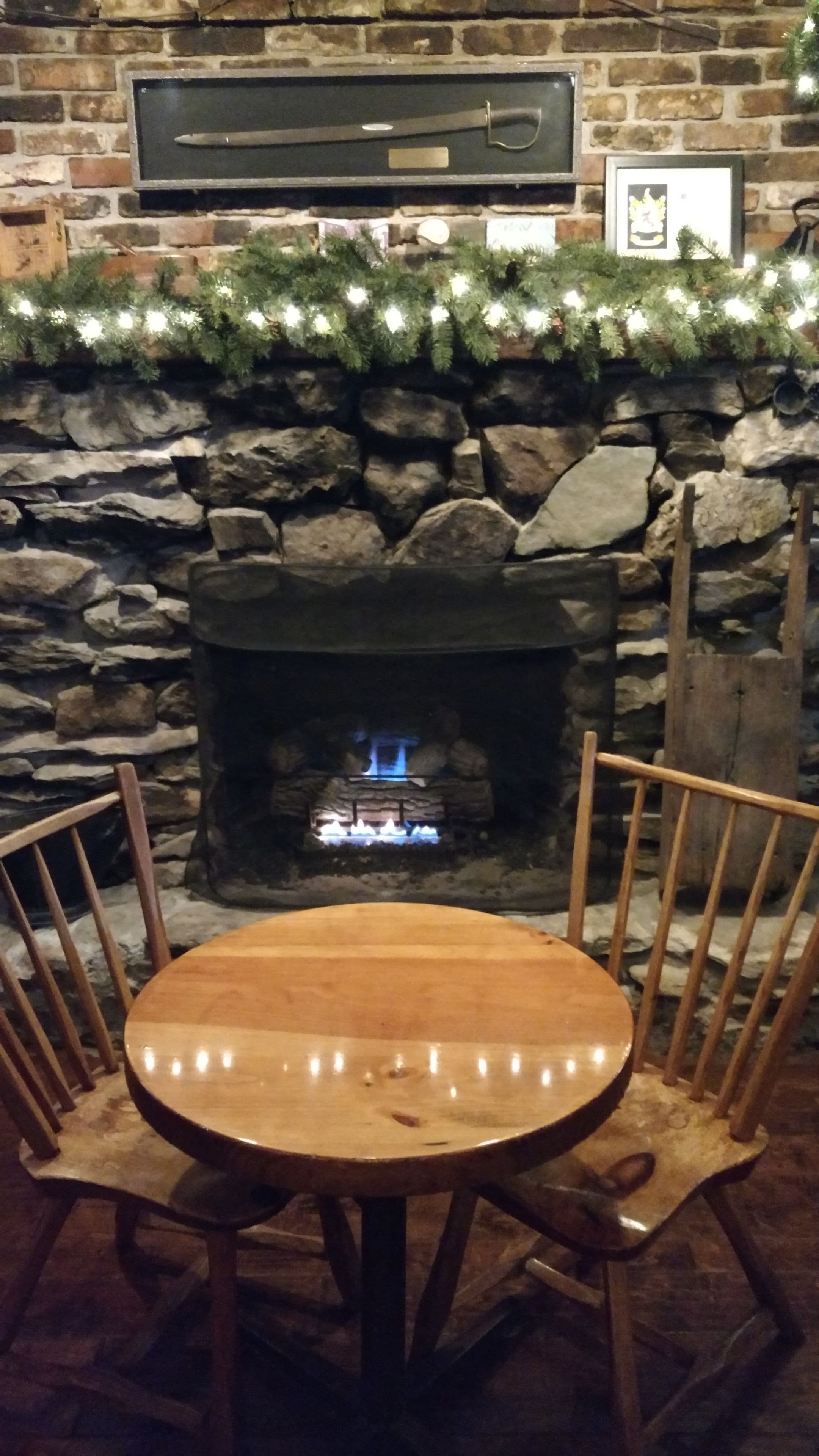 A stone fireplace with a fire, a wooden table, and chairs in front.