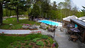 A pool area with lounge chairs and umbrellas, surrounded by landscaped gardens and a building with large windows. - Summit Lodge (Killington)