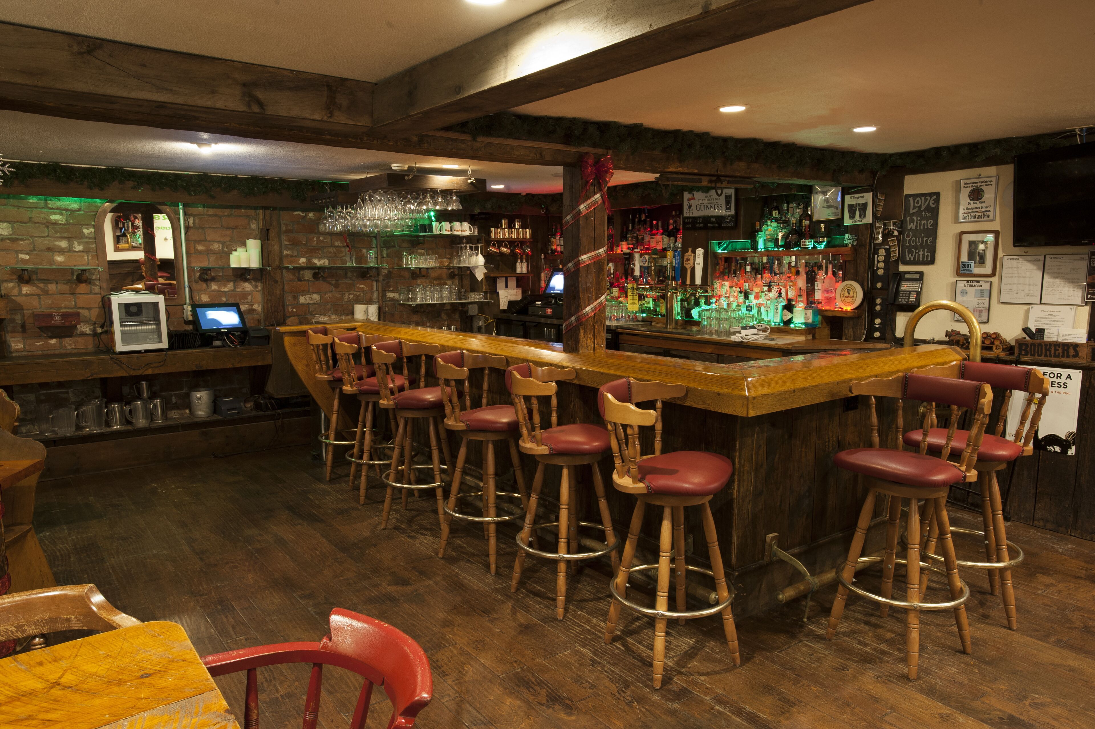 A bar area with wooden stools, a bar counter, and shelves stocked with bottles and glasses.