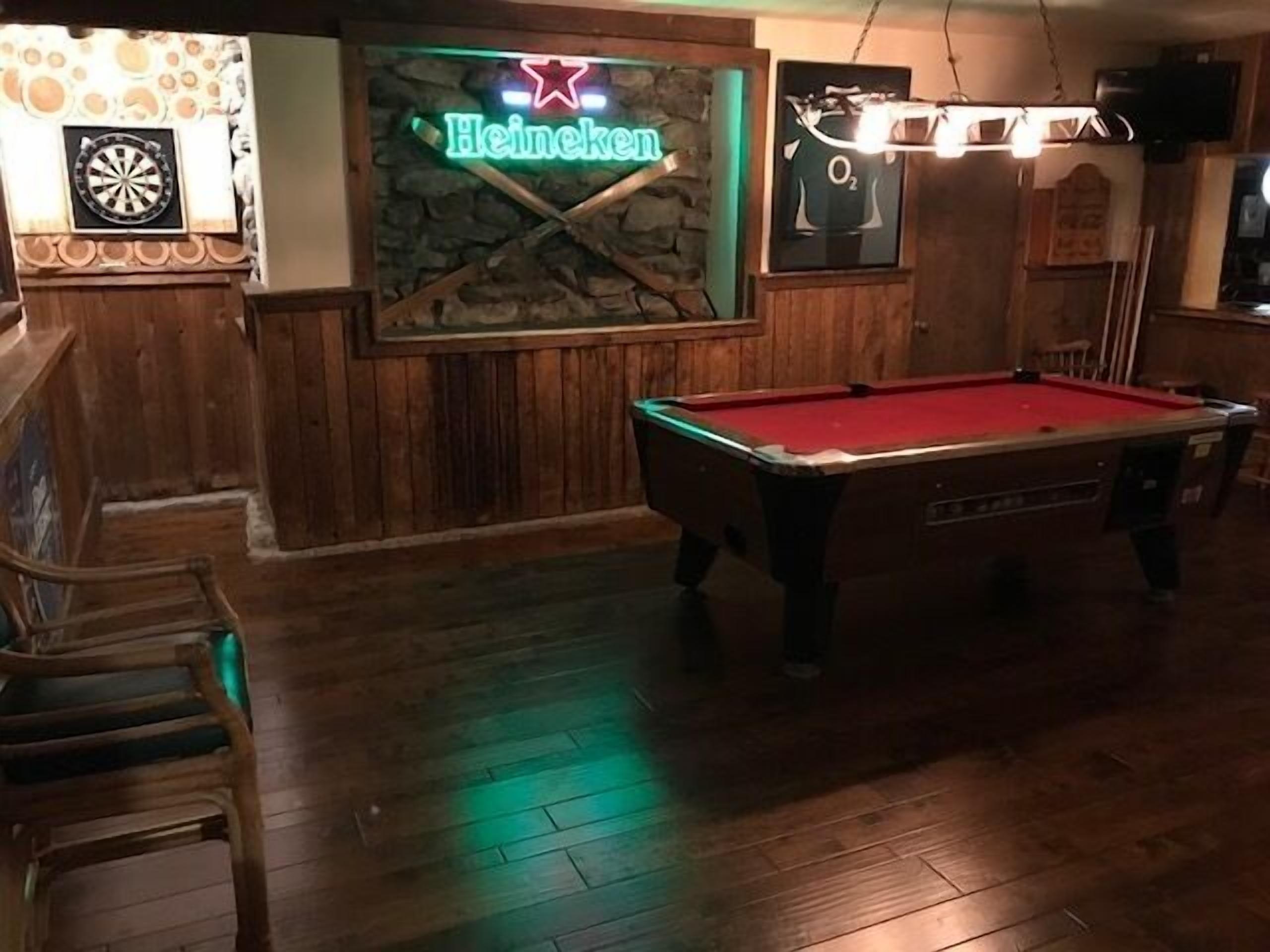 Une table de billard dans une pièce aux murs en bois, avec une enseigne Heineken.