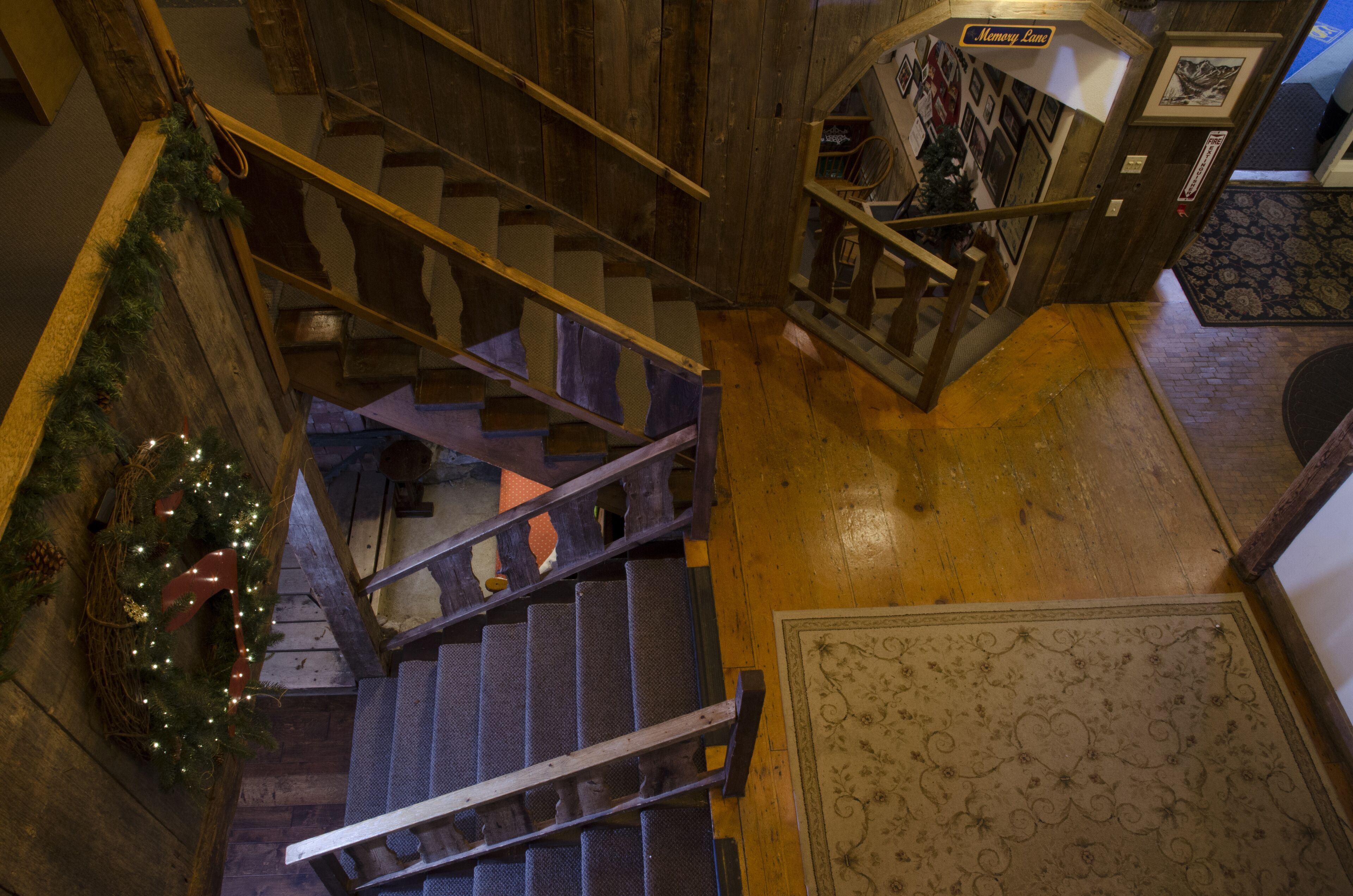 A wooden staircase with a railing, a Christmas wreath, and a patterned rug on the floor.