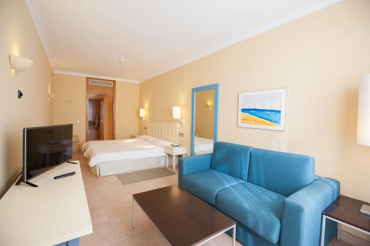 A hotel room with a TV, a blue sofa, a bed, a desk, and a bathroom.