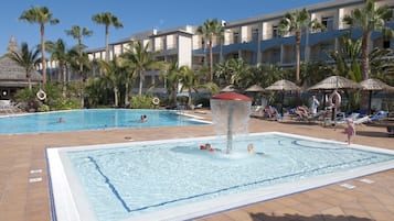 Zona de piscina de hotel con varias piscinas, palmeras y sillas de descanso.